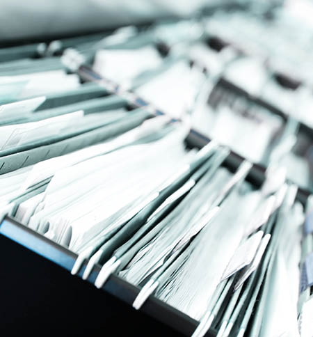 Multiple rows of filing cabinets in an office or medical establishment, overflowing with files. Narrow depth of field to emphasize the “neverending" feeling